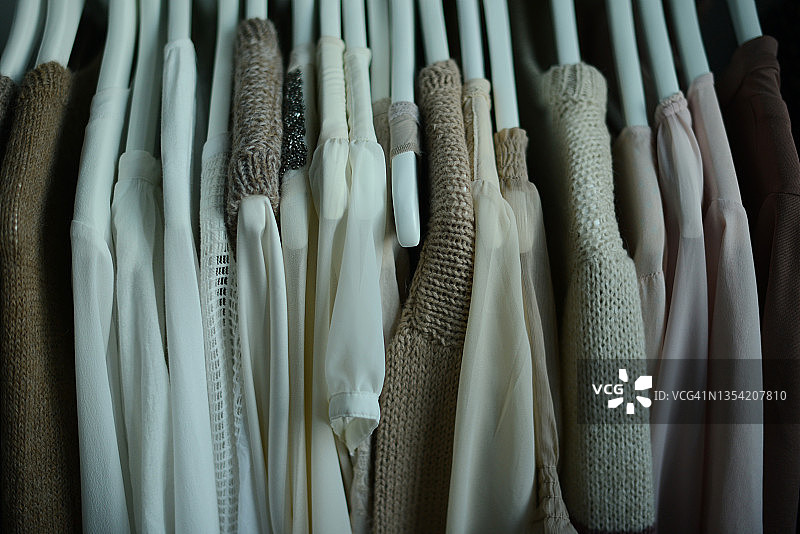 一排挂在衣架上的自然色调衬衫和针织毛衣图片素材