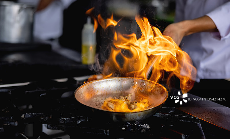 厨师在餐厅厨房的平底锅上火焰烹饪食物的特写图片素材