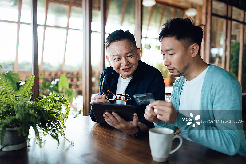 快乐的亚洲老年父亲和儿子一起使用平板电脑在网上购物，并在家里用信用卡进行在线支付图片素材