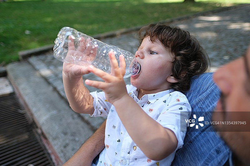 小孩正在喝瓶子里的纯净水，炎热的夏日图片素材