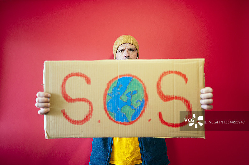 男人拿着写有S.O.S.的纸板标牌，O是地球图片素材