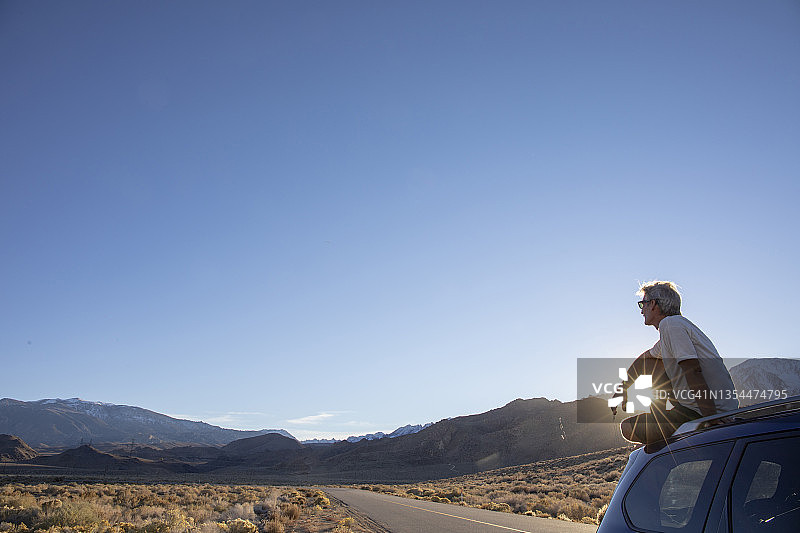 男子在停在沙漠公路旁的汽车顶部放松图片素材