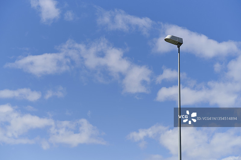 矩形金属路灯与蓝色天空和白色云朵的仰视角度图片素材