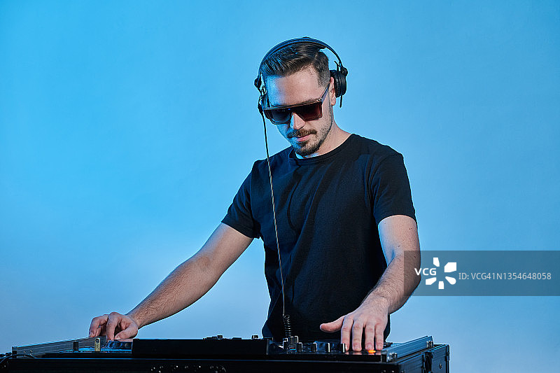 在蓝色灯光背景下进行表演的年轻男性DJ图片素材