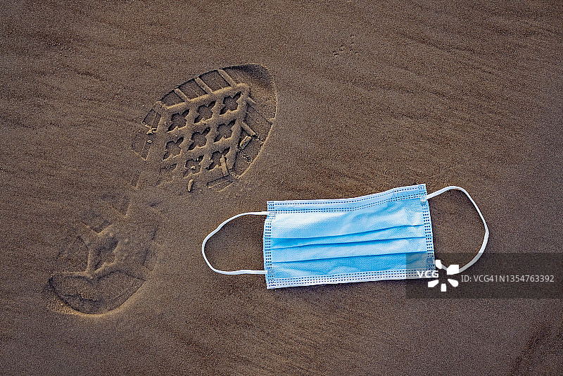 沙滩上的蓝色医用口罩和鞋印图片素材