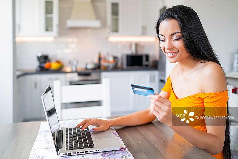 手持信用卡在笔记本电脑上打字的微笑年轻女子图片素材
