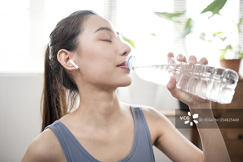 运动后饮水有助于维持血压，年轻女人在公寓锻炼或瑜伽后饮水图片素材