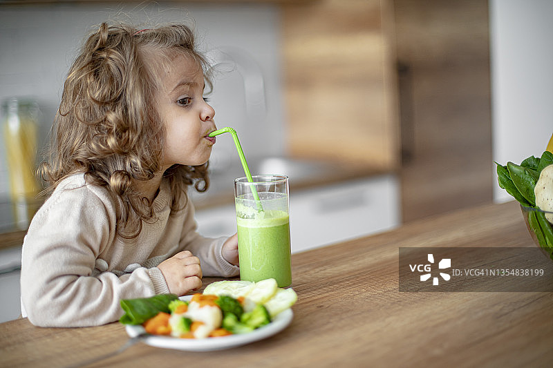 可爱的小女婴喝绿色冰沙和吃蔬菜图片素材