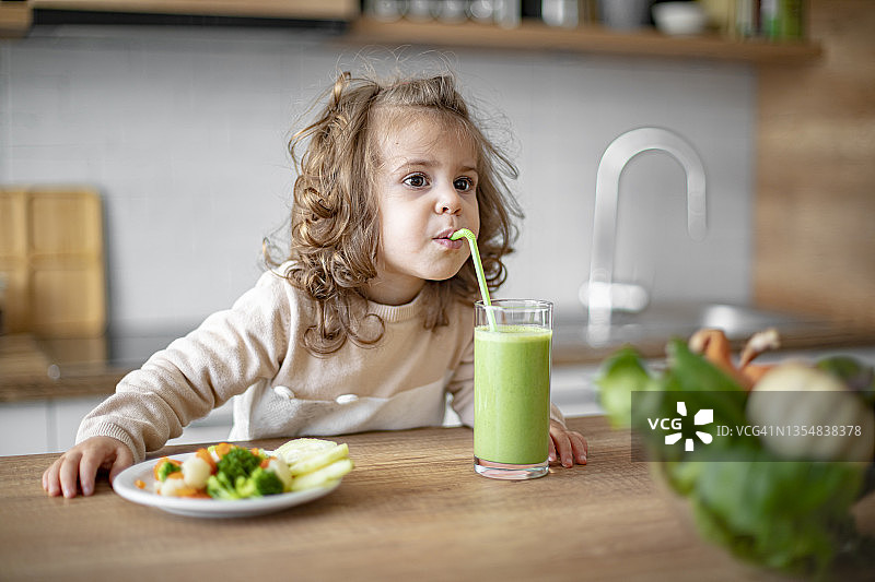 可爱的小女婴喝绿色冰沙和吃蔬菜图片素材