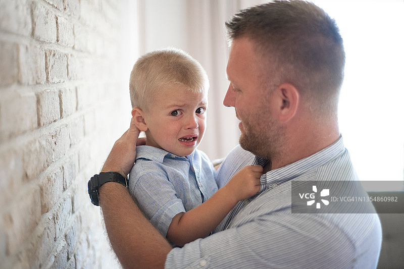 年轻父亲安慰哭泣并看着镜头的儿子图片素材