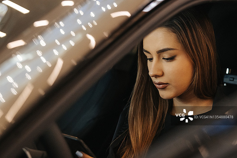 优雅时尚的年轻女人在豪华轿车驾驶座上使用手机图片素材