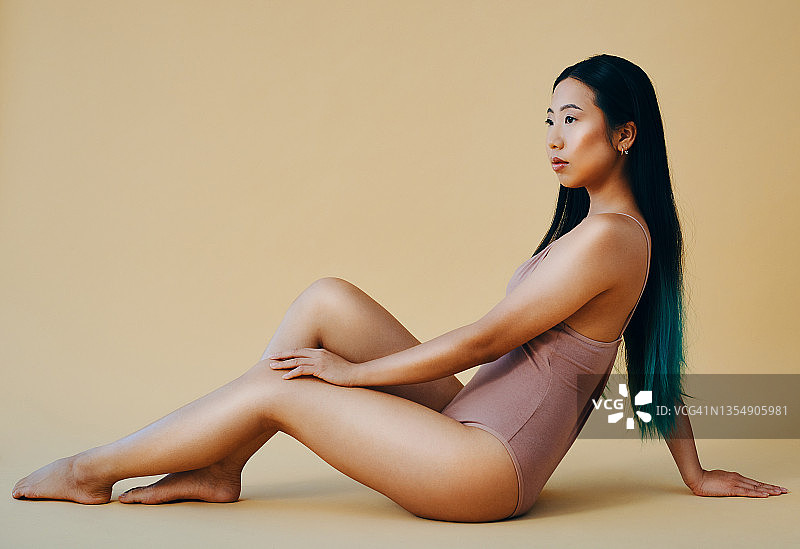 一位有魅力的年轻女子独自坐在工作室里摆姿势的全身照图片素材