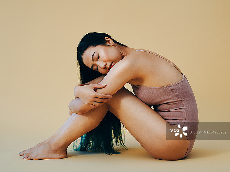 一位有魅力的年轻女子独自坐在工作室里摆姿势的全身照图片素材