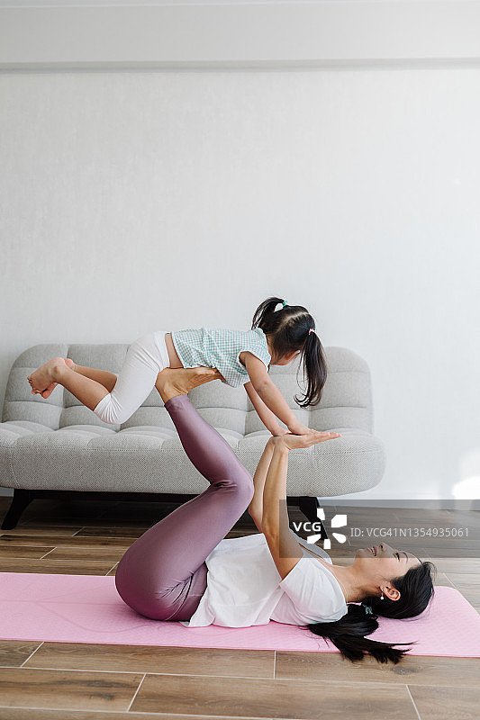 亚洲小女孩和年轻妈妈在家里的粉色垫子上做瑜伽图片素材