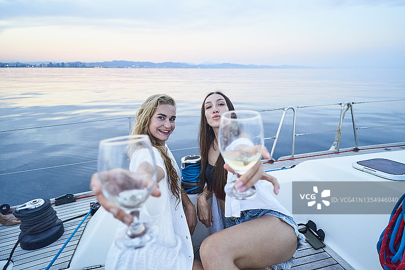 两名女子乘帆船旅行时，举着酒杯对着镜头的特写图片素材