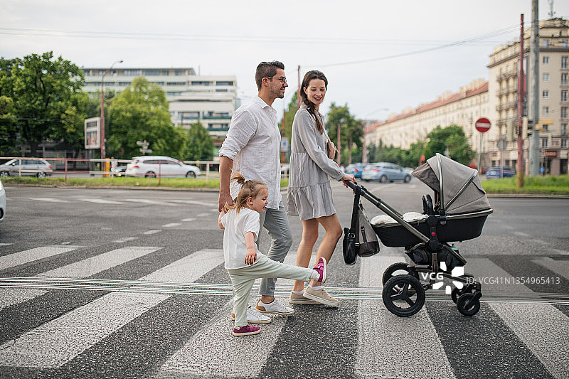 幸福的年轻家庭推着婴儿车，带着小女儿在城镇的斑马线上图片素材