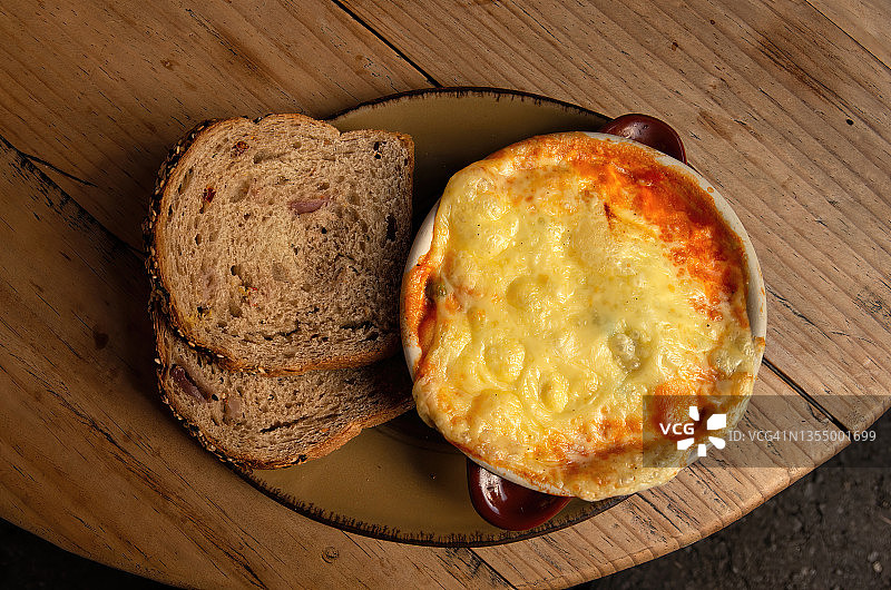 配有融化奶酪和土豆泥的牧羊人派，配切片面包，在木制咖啡桌上图片素材