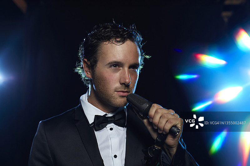 穿着西装和领结，拿着麦克风，背景为迷幻光晕的男人肖像图片素材