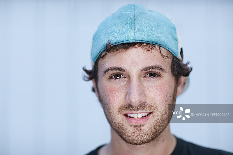 看着镜头微笑、戴着反戴帽子的年轻男子头像图片素材