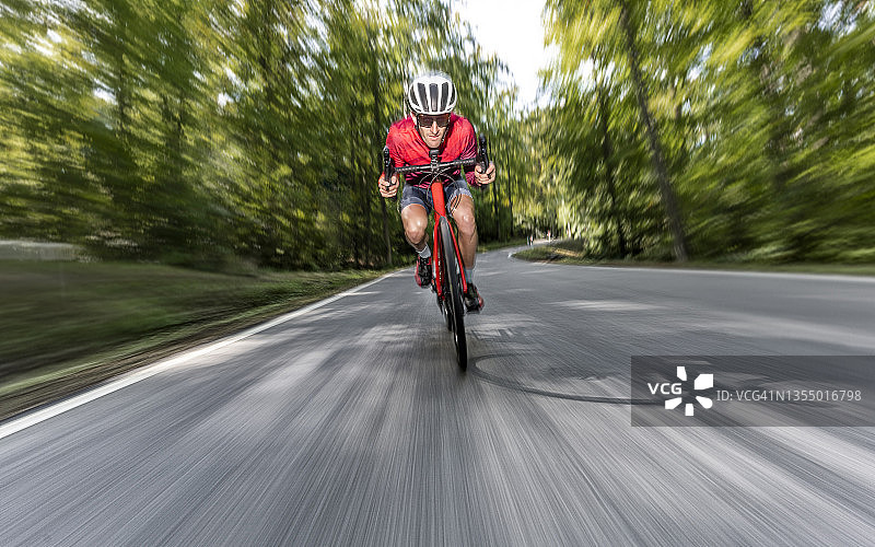 骑自行车行驶在森林沥青路上的男人图片素材