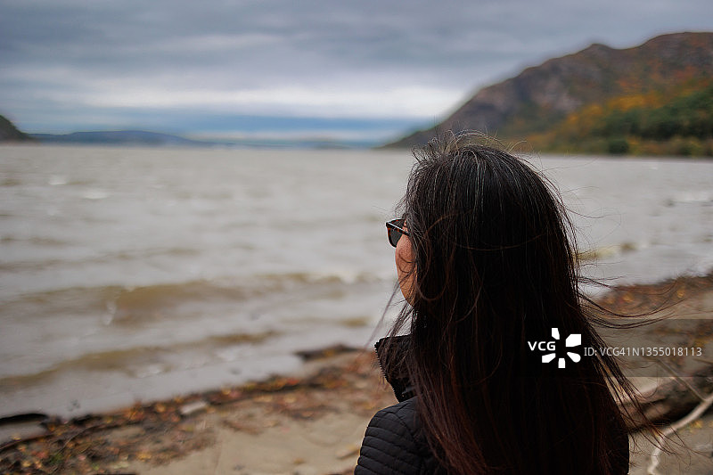 女人站在岸边观赏波光粼粼的海面，海浪拍打着海岸图片素材