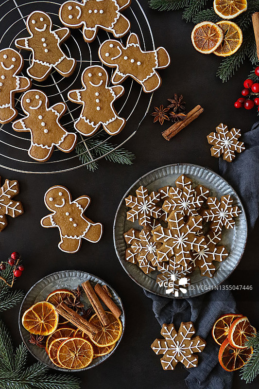 金属丝圆形冷却架上摆放着新鲜出炉的自制姜饼人饼干，白色皇家糖霜装饰，冬青叶和星星饼干，灰色薄纱，肉桂棒，柑橘干，黑色背景图片素材