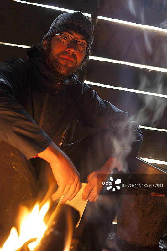 男子坐在老挝丰沙里省班蓬洪的家中火炉旁图片素材