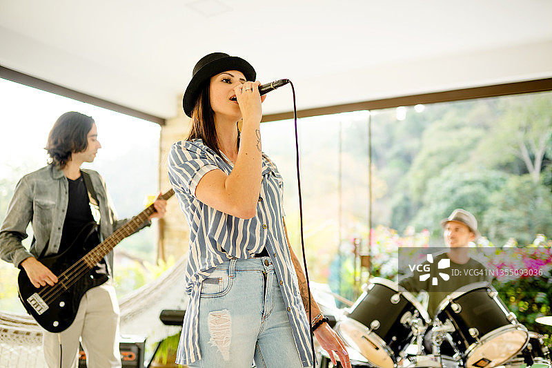 年轻女人在乐队排练时对着麦克风唱歌图片素材