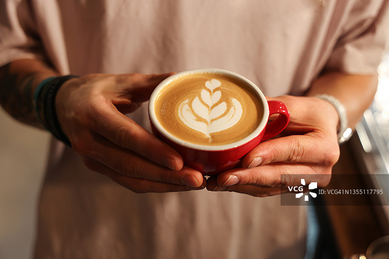 咖啡师提供带有花卉图案奶泡的拿铁咖啡图片素材