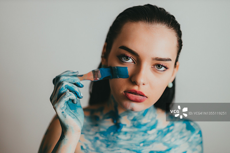女人用刷子在脖子和脸上涂蓝色人体彩绘图片素材