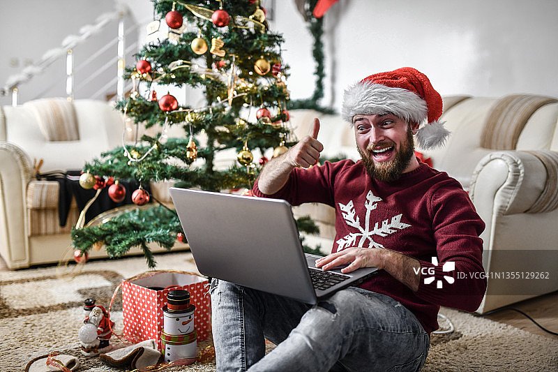 面带微笑的男性在圣诞树下使用笔记本电脑顺利进行视频会议图片素材