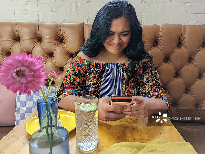 在餐厅里用手机微笑的年轻女人图片素材