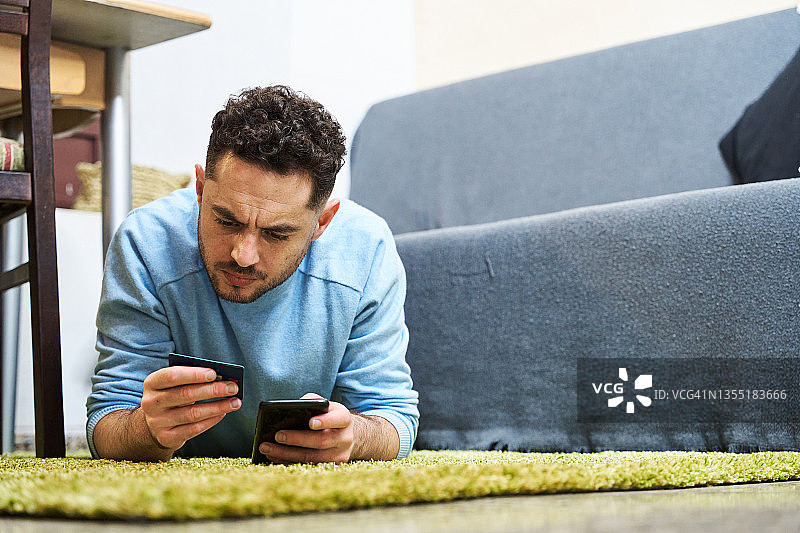 男子躺在客厅地毯上用手机查看银行账单图片素材