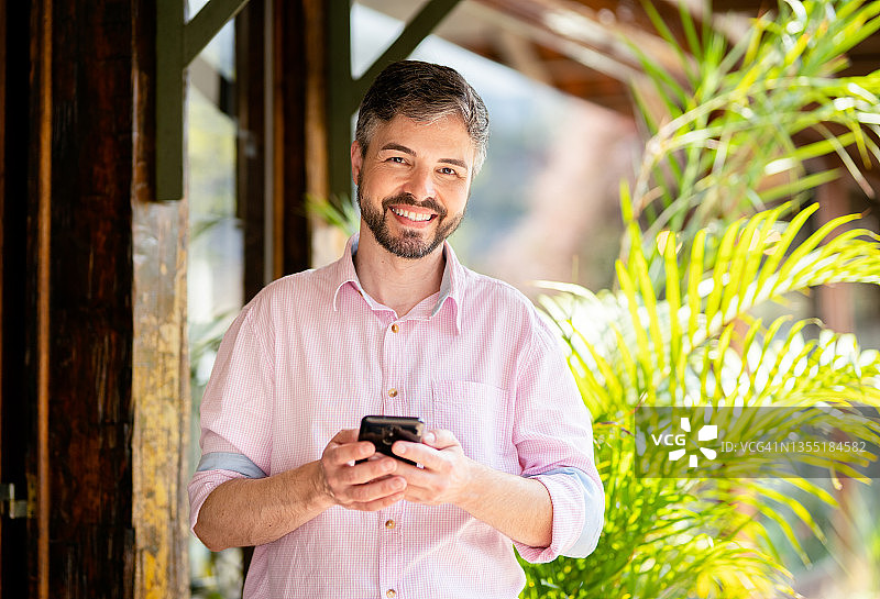在商店外查看手机的微笑男人图片素材