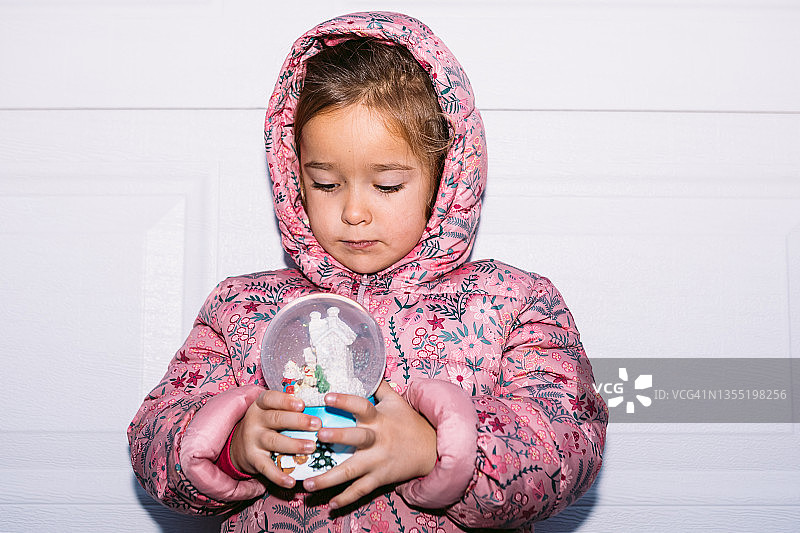 小女孩身穿粉色外套和帽子，手持圣诞水晶球图片素材