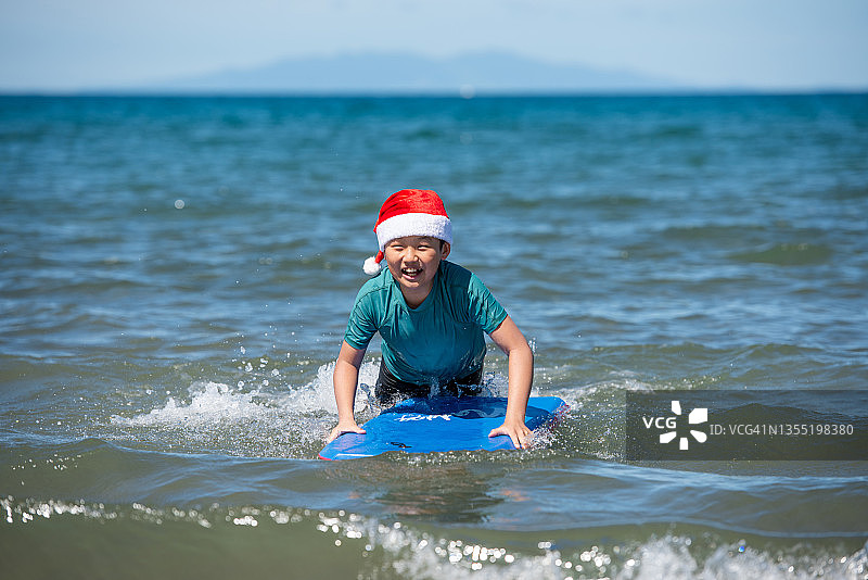 戴着圣诞帽的青少年在海滩上冲浪，享受夏季圣诞节图片素材