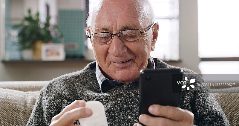 老年男子在家中使用手机时阅读药品容器标签的照片图片素材