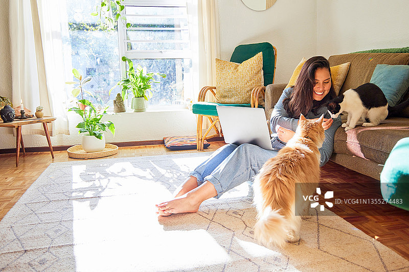 年轻女子和她的猫坐在客厅里使用笔记本电脑全身照图片素材