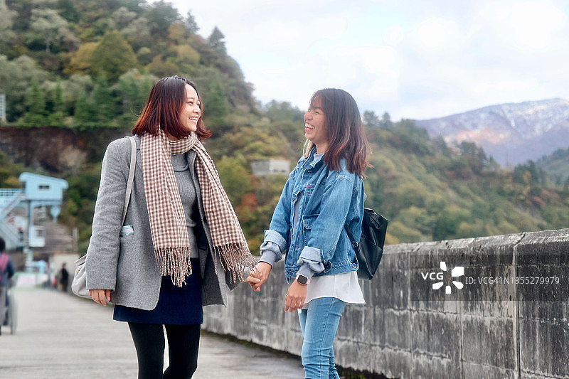 年轻的亚洲学生在秋天的湖边散步图片素材