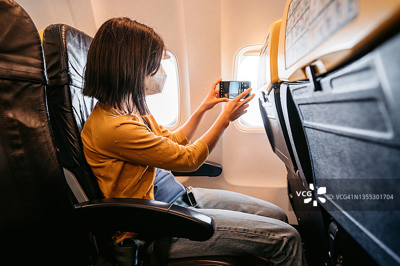 戴着口罩在飞机上隔着窗户拍照的女人图片素材