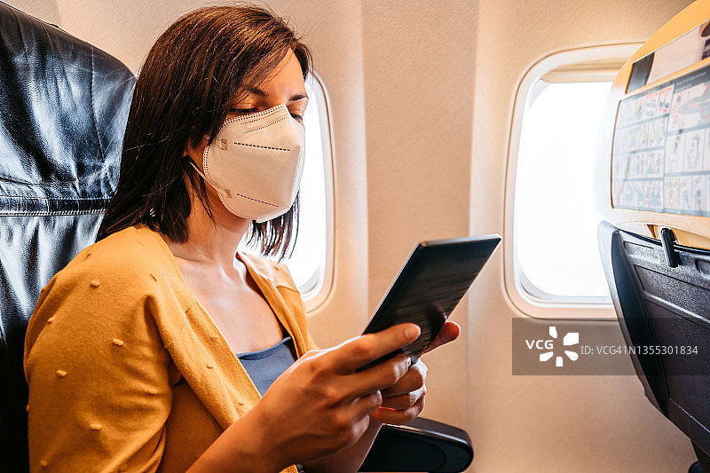 在飞机上使用平板电脑的戴口罩女人图片素材
