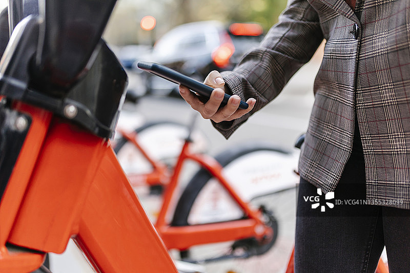 女人使用智能手机上的二维码在城市租自行车图片素材