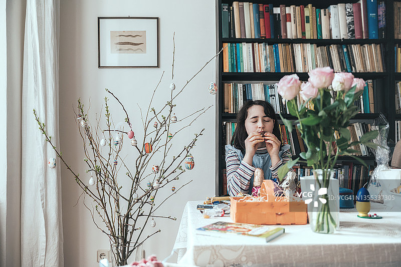 小女孩在桌旁从复活节篮子里吃巧克力图片素材