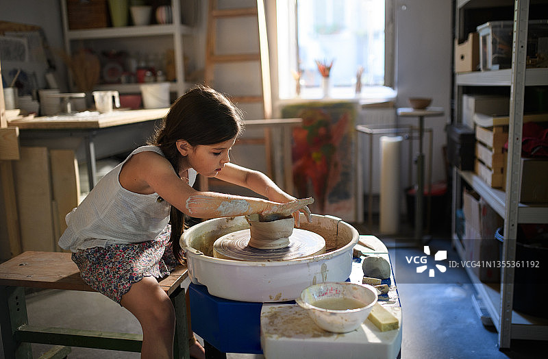 在艺术工作室里在陶轮上制作陶器的小女孩的侧视图图片素材