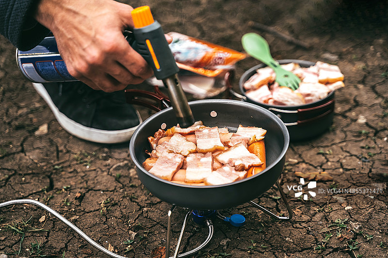 男人在带有便携式燃烧器的燃气锅中烹饪和烤培根图片素材