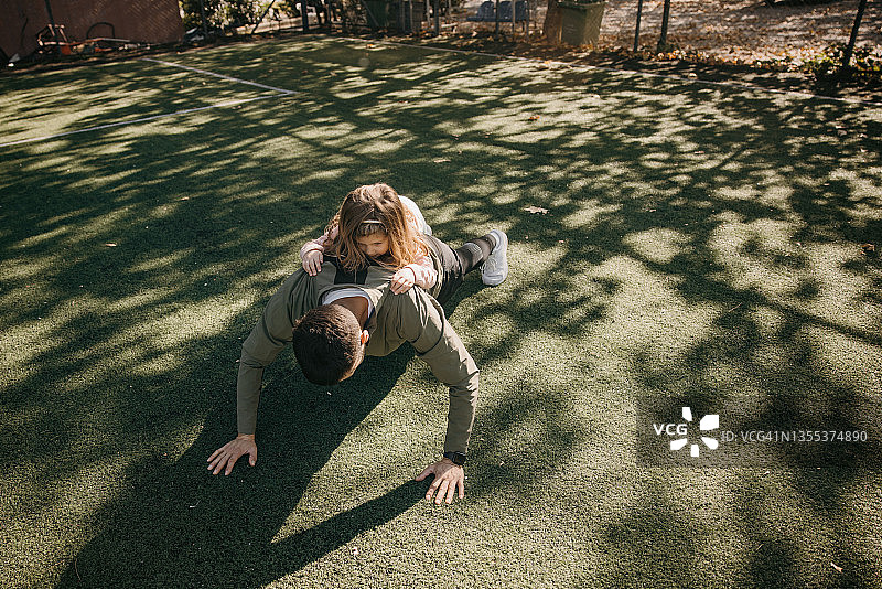 男人在足球场上做俯卧撑，女儿趴在他背上图片素材