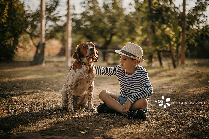 小男孩坐在后院的草地上，抚摸他的小狗图片素材