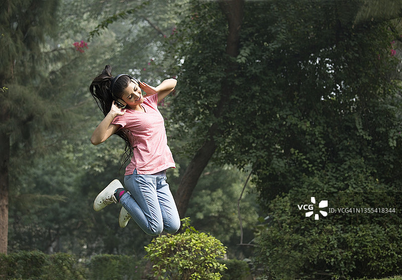 在公园听音乐时跳跃的快乐女人图片素材