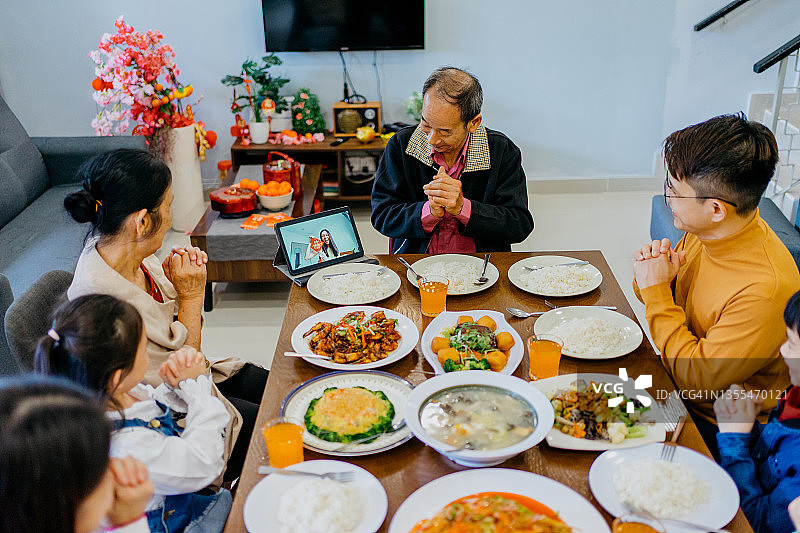 快乐的亚裔中国家庭在团圆晚宴期间使用数码平板电脑与亲戚进行视频通话图片素材