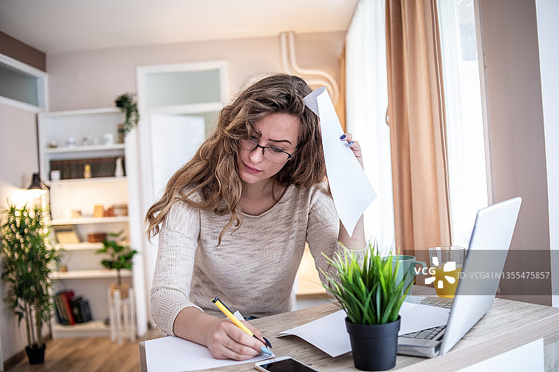 使用笔记本电脑和纸张学习的年轻女学生图片素材